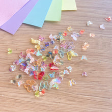 Load image into Gallery viewer, Colourful butterfly-shaped embellishments on a wooden surface with colourful paper sheets in the background.
