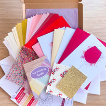 Load image into Gallery viewer, Collection of colourful paper craft supplies with an iris folding guide on a wooden surface
