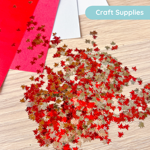 Red and silver leaf confetti on a wooden surface with craft supplies in the background.