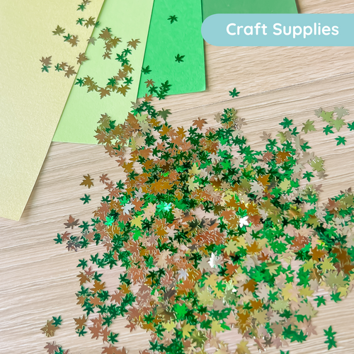 Colorful leaf-shaped confetti on a wooden surface with craft supplies in the background.