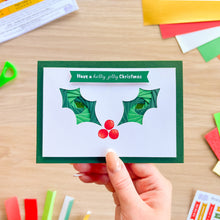 Load image into Gallery viewer, A hand holds a greeting card with an iris fold holly leave design with printed red holly berries and 'Have a holly jolly Christmas' greeting.
