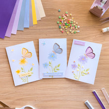 Load image into Gallery viewer, Three iris fold butterfly cards made with the aperture pack laid on a wooden table with craft materials.
