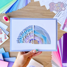 Load image into Gallery viewer, A half-rainbow iris folding card. The other half of the card is made of lots of punched paper hearts.
