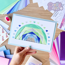 Load image into Gallery viewer, A full iris folding rainbow in blues and greens with an arc of punched paper hearts
