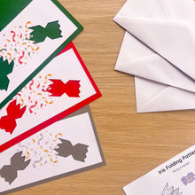 Load image into Gallery viewer, Three party cracker cut-outs on coloured card with white envelopes on a light wood surface next to a printed iris folding pattern sheet.
