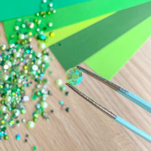 Load image into Gallery viewer, Tweezers holding a green gemstone with green glitter on a wooden
