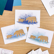 Load image into Gallery viewer, Three printed cards featuring watercolor polar bear illustrations in blue tones with bear cutouts, arranged on a light wood tabletop with paper swatches and envelopes nearby.
