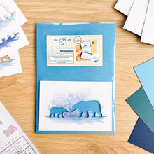Load image into Gallery viewer, A Polar Bear &amp; Cub aperture card pack in poly wrap, displayed on a wooden table with other crafting materials scattered around it.
