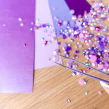 Load image into Gallery viewer, Close-up of gems and tweezers on a wooden surface with purple paper.
