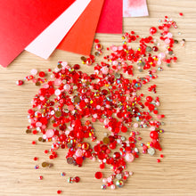 Load image into Gallery viewer, Red and pink gemstones on a wooden surface with red paper in the background
