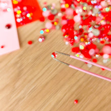 Load image into Gallery viewer, Close-up of tweezers holding a single red gem
