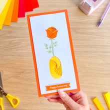 Load image into Gallery viewer, Hand holding an iris folded card with a rose design and 'Happy Anniversary' text on a wooden table.
