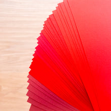 Load image into Gallery viewer, Stack of red paper sheets on a wooden surface
