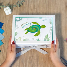 Load image into Gallery viewer, Box with a turtle design and &#39;Just Keep Swimming&#39; text held by hands on a wooden surface.
