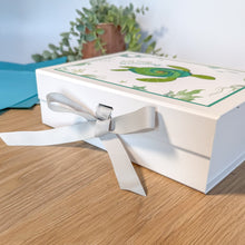 Load image into Gallery viewer, Gift box with a white ribbon on a wooden surface with a blurred plant in the background
