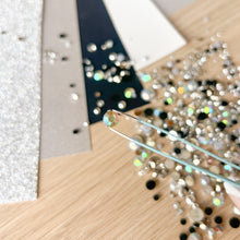 Load image into Gallery viewer, Close-up of a hand using tweezers to handle small rhinestones on a wooden surface.
