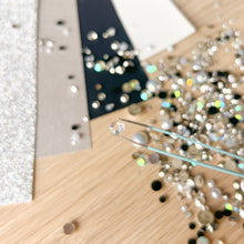 Load image into Gallery viewer, Close-up of a wooden surface with scattered rhinestones and a pair of tweezers.
