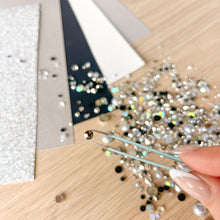 Load image into Gallery viewer, Person using tweezers to handle rhinestones on a wooden surface.
