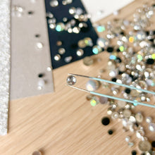 Load image into Gallery viewer, Close-up of tweezers holding a diamond next to a pile of diamonds on a wooden surface.

