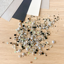 Load image into Gallery viewer, Scattered silver rhinestones on a wooden surface with color swatches in the background
