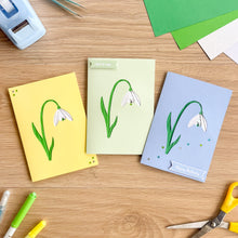 Load image into Gallery viewer, Three greeting cards with floral snowdrop designs on a wooden surface with stationery items.
