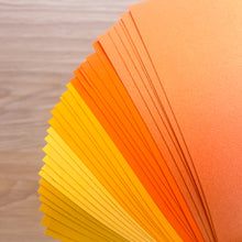 Load image into Gallery viewer, Stack of orange and yellow paper sheets on a wooden surface
