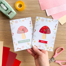 Load image into Gallery viewer, Two mushroom-themed cards on a wooden table with stationery items.
