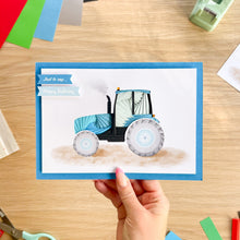 Load image into Gallery viewer, A hand holds an iris fold birthday card featuring a blue and white tractor illustration, with a blue border and a 'Just to say' and 'Happy Birthday' banners.
