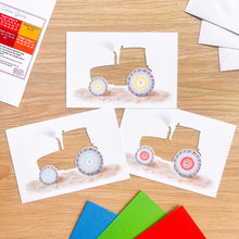 Load image into Gallery viewer, Three printed card apertures featuring watercolor-style tractors on a light wood tabletop, with colored paper squares and white envelopes partially visible around them.
