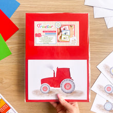 Load image into Gallery viewer, A hand holds a red 'Tractor' card aperture pack on a light wood table, surrounded by colorful paper sheets and printed cards.
