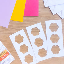 Load image into Gallery viewer, Flower-shaped cutouts on white paper with colorful cards in the background
