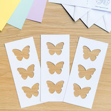 Load image into Gallery viewer, Butterfly-shaped paper cut-outs on white paper against a wooden background
