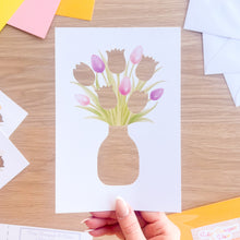 Load image into Gallery viewer, Card with a cut-out vase of tulips held by a hand on a wooden surface with envelopes.
