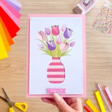 Load image into Gallery viewer, Hand holding an iris fold card with a floral design on a wooden table with craft supplies.
