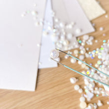 Load image into Gallery viewer, Pearl being held by tweezers with scattered pearls on a wooden surface
